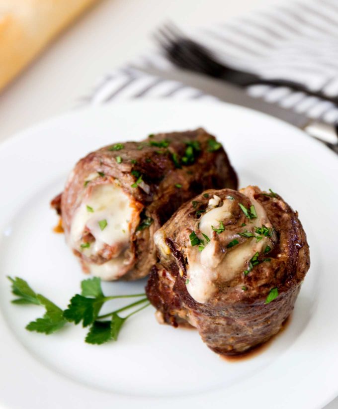 Cooked Italian stuffed flank steak on white plate with parsley