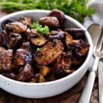 White bowl of roasted mushrooms with silverware