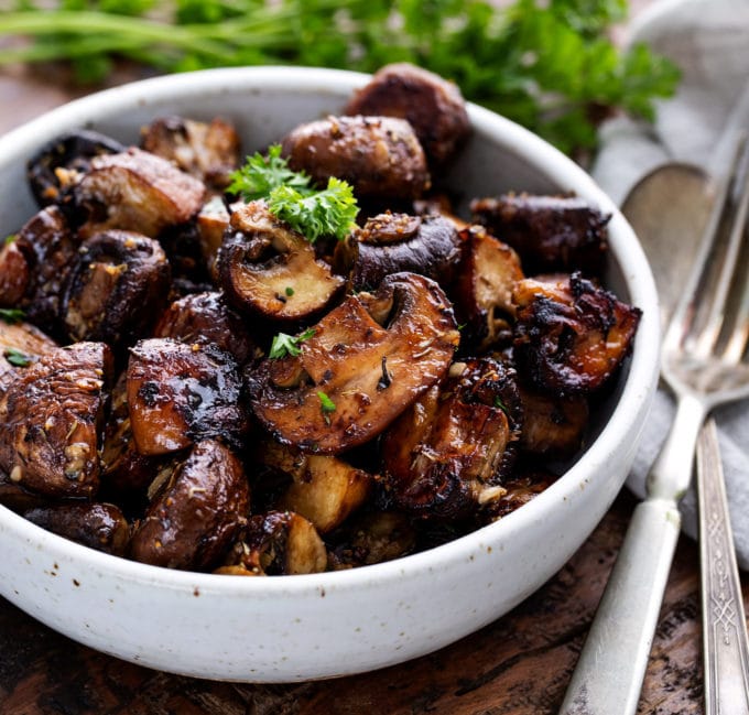 White bowl of roasted mushrooms with silverware
