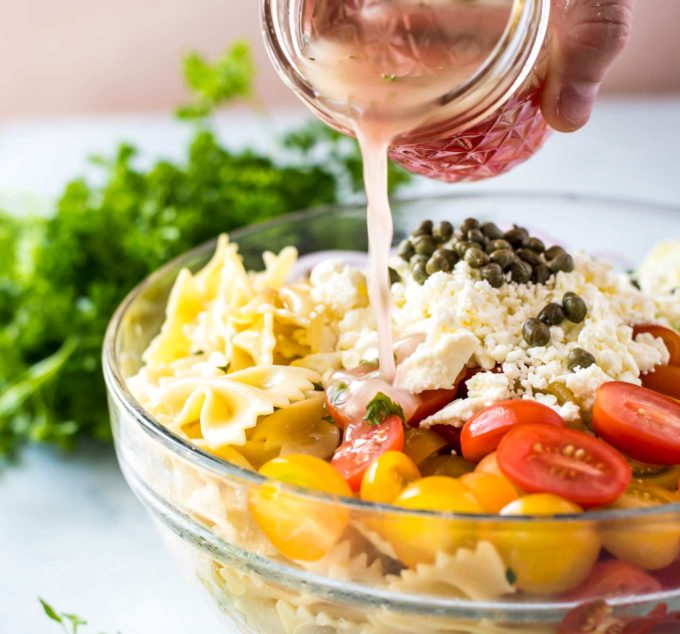 Pouring homemade dressing onto pasta salad