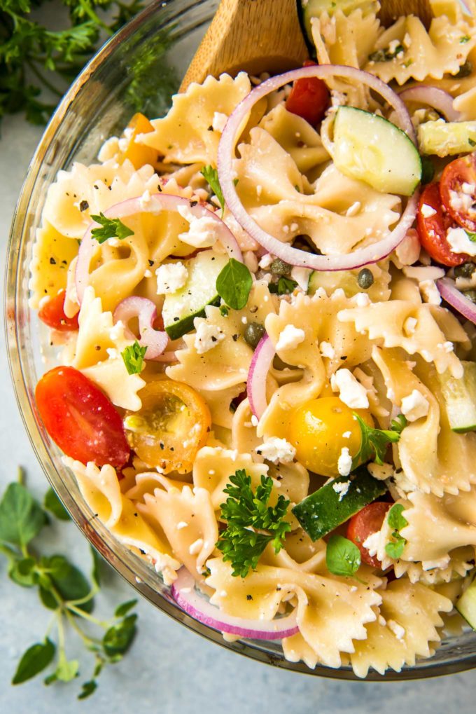 Always a crowd-pleaser, this pasta salad has won first place in several potluck contests.ย Summer vegetables, tender pasta, salty cheese, and a mouthwatering zesty dressing! #pastasalad #potluck #bbq #italian #greek #mediterranean #pasta, #salad #makeaheadrecipe #easyrecipe Serving pasta salad from bowl