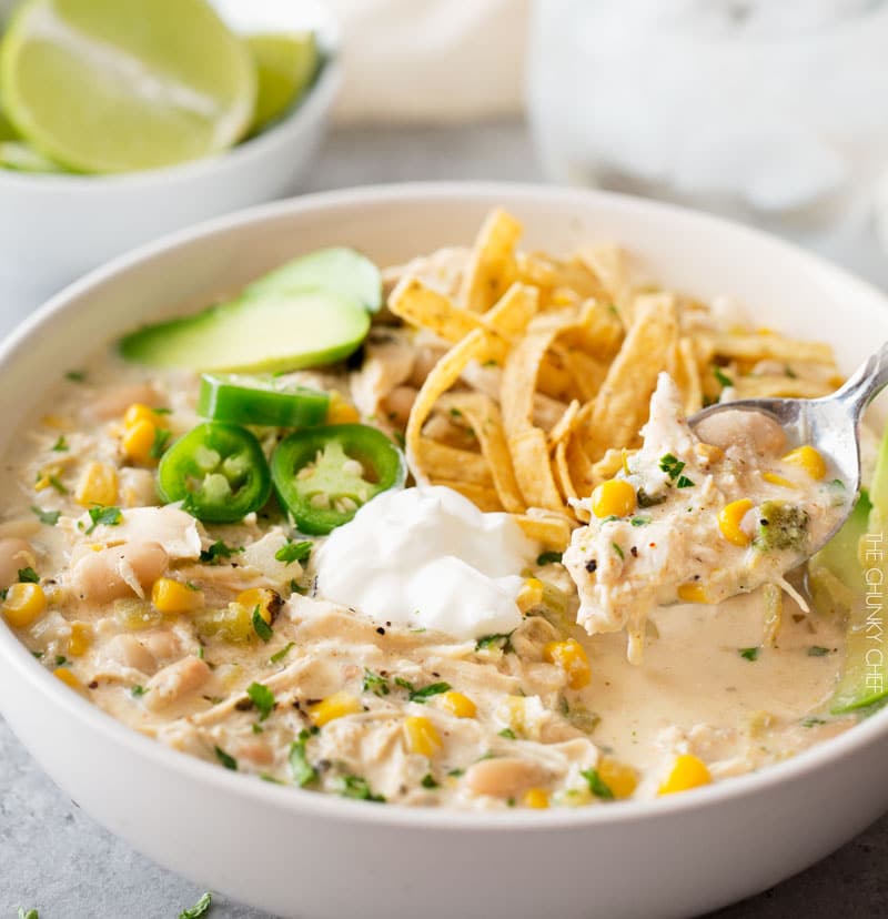 Spoon of crockpot white chicken chili with garnishes