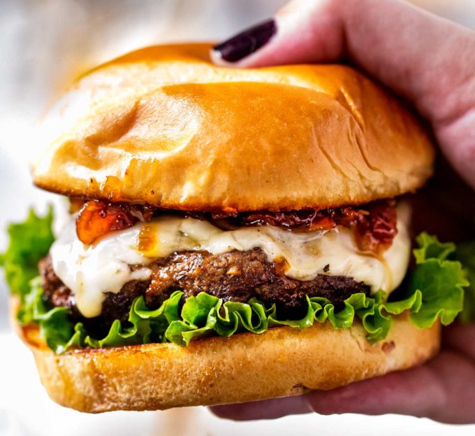 hand holding a cheeseburger topped with bacon jam