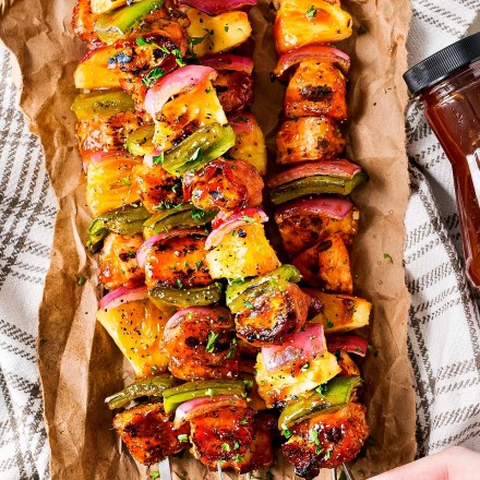 holding a skewer of grilled chicken with pineapple and peppers