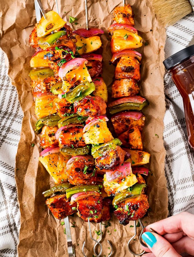 holding a skewer of grilled chicken with pineapple and peppers