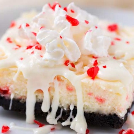 Peppermint White Chocolate Cheesecake Bars | An Oreo cookie crust, velvety smooth white chocolate peppermint cheesecake filling, candy cane pieces, and an extra drizzle of creamy white chocolate.  Holiday baking at it's finest! | The Chunky Chef | #cheesecakerecipes #cheesecakebars #peppermint #whitechocolate #holidaybaking #Christmasdesserts