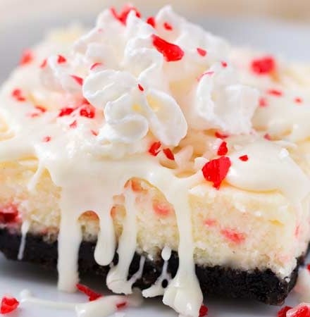 Peppermint White Chocolate Cheesecake Bars | An Oreo cookie crust, velvety smooth white chocolate peppermint cheesecake filling, candy cane pieces, and an extra drizzle of creamy white chocolate.  Holiday baking at it's finest! | The Chunky Chef | #cheesecakerecipes #cheesecakebars #peppermint #whitechocolate #holidaybaking #Christmasdesserts