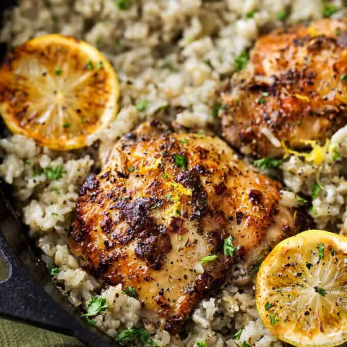 greek lemon chicken and rice in a cast iron skillet with charred lemons
