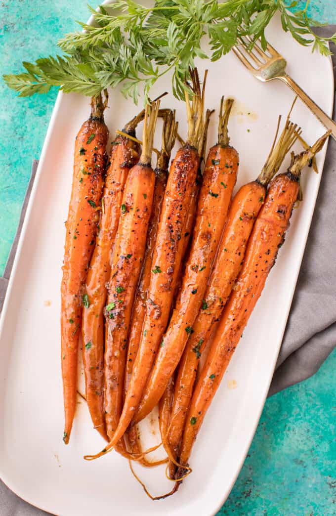 Tender baby carrots are coated in a sweet and savory glaze, then "roasted" in the crockpot! Free up your oven with this EASY side dish that's perfect for the holidays! | #carrots #sidedish #holidaysidedish #holidayrecipe #slowcookercarrots #crockpotcarrots group of glazed carrots on white platter