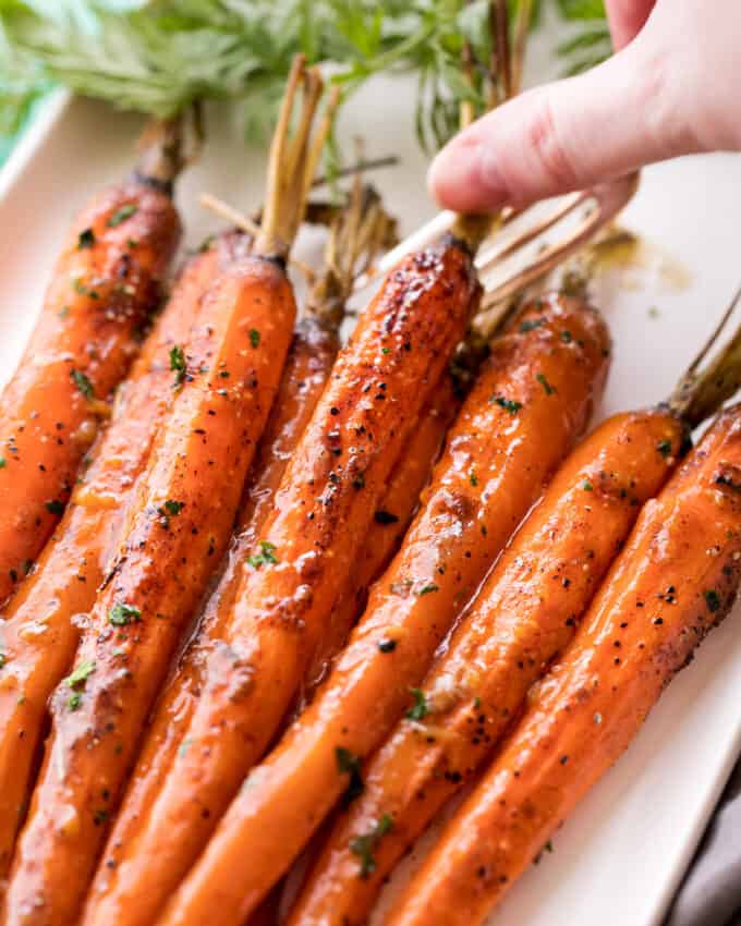 using a fork to pick up glazed carrots from platter