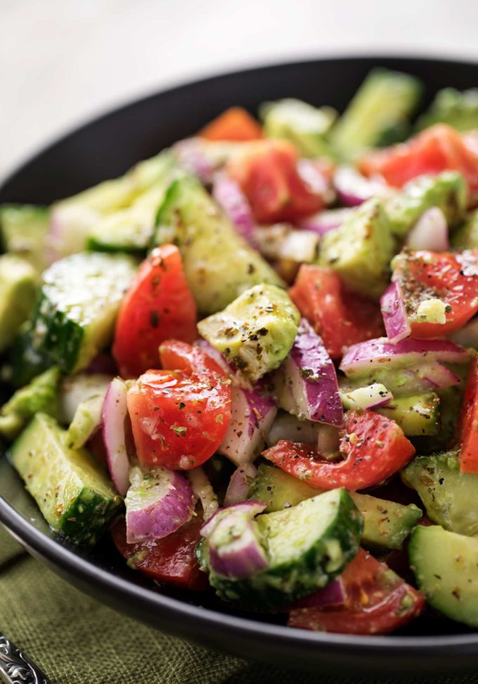 Tomato avocado salad with greek dressing in black bowl