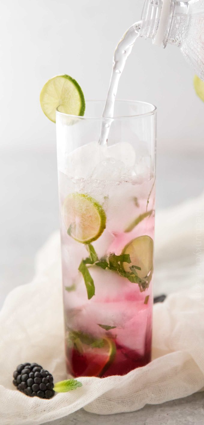 Pouring club soda in blackberry mojito