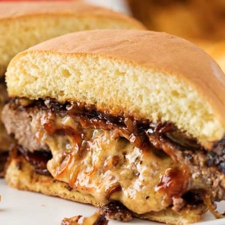 This classic Juicy Lucy burger is a well known Midwestern recipe.  Definitely not your average cheeseburger, this burger recipe is stuffed with caramelized onions and cheddar cheese!  Our favorite version also includes crispy bacon and smoky bbq sauce! #burger #cheeseburger #juicylucy #cheddar #baconcheeseburger #stuffed #summerbbq