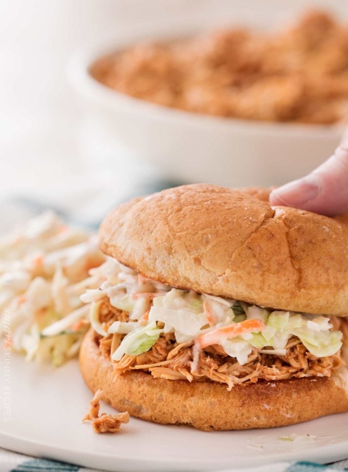 Sandwich of bbq pulled chicken with coleslaw on white plate