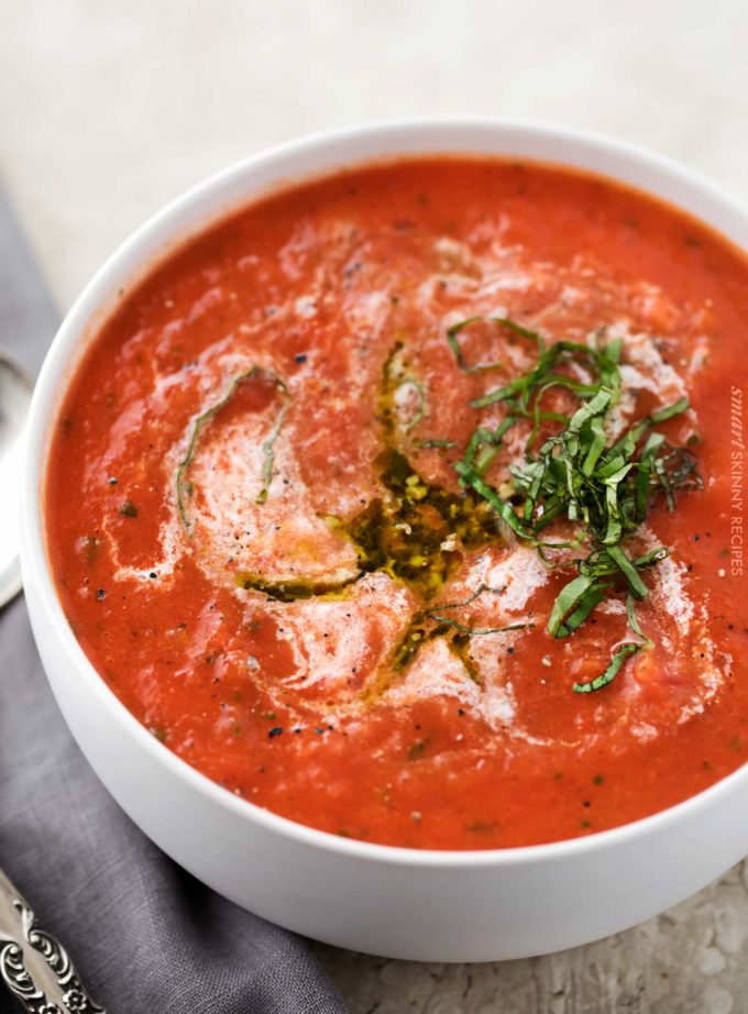 Tomato basil soup in white bowl with drizzle of pesto and cream