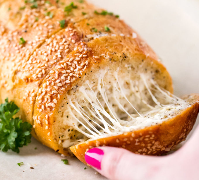 Pulling a slice of cheesy garlic bread from loaf