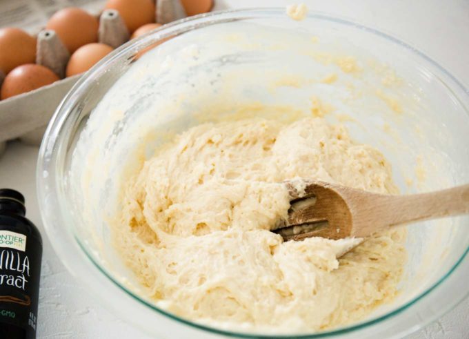 Mixing up donut holes batter in clear mixing bowl with wooden spoon