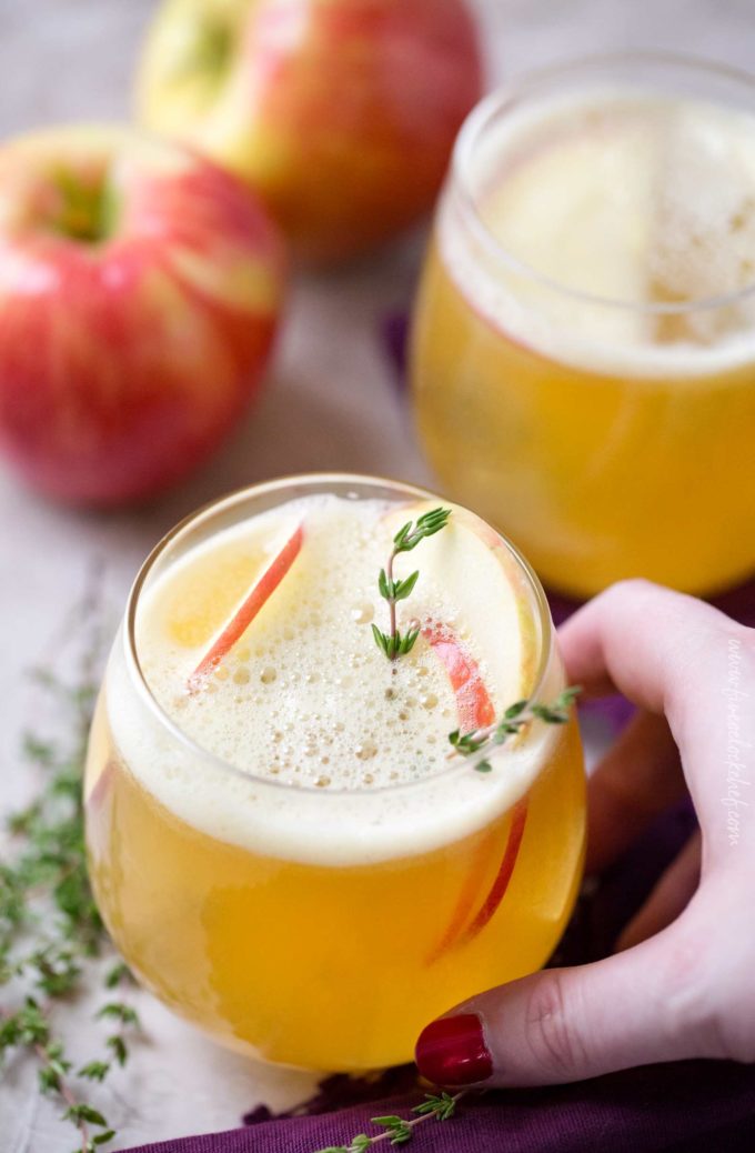 Holding a bourbon cocktail with apples and thyme in stemless glass