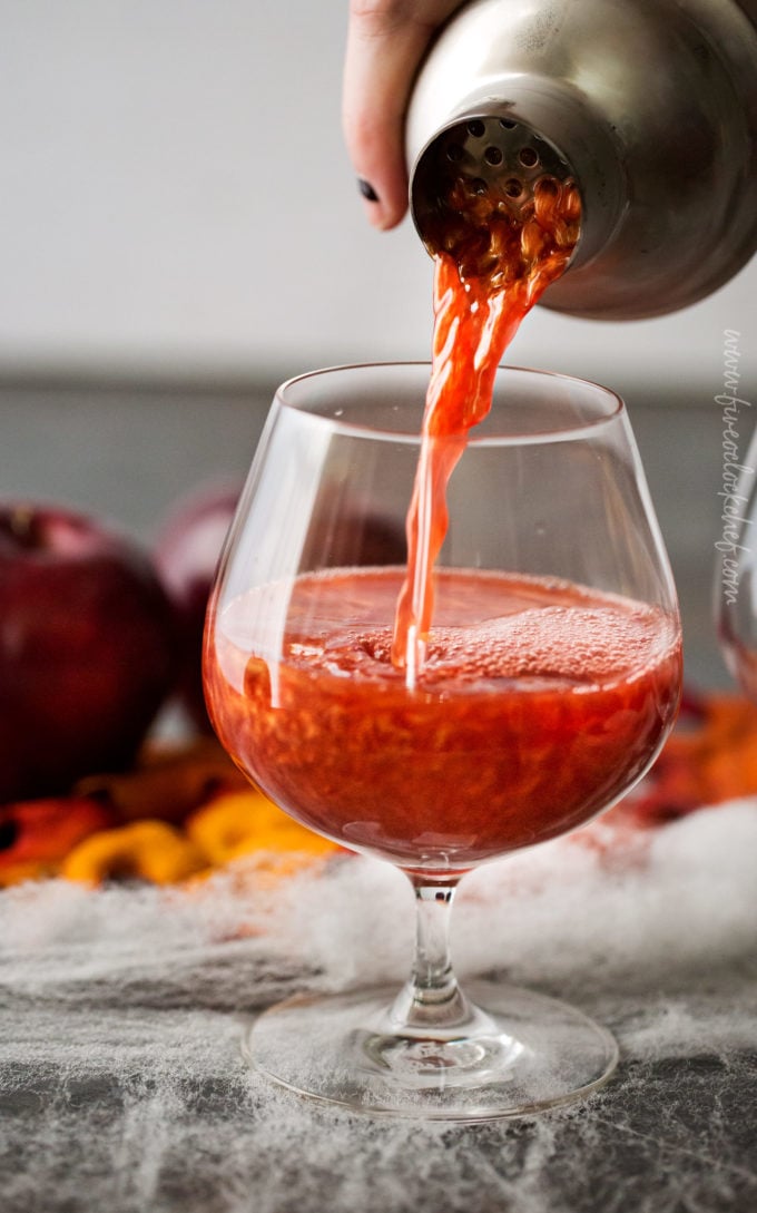 Pouring apple cider cocktail from cocktail shaker into glass