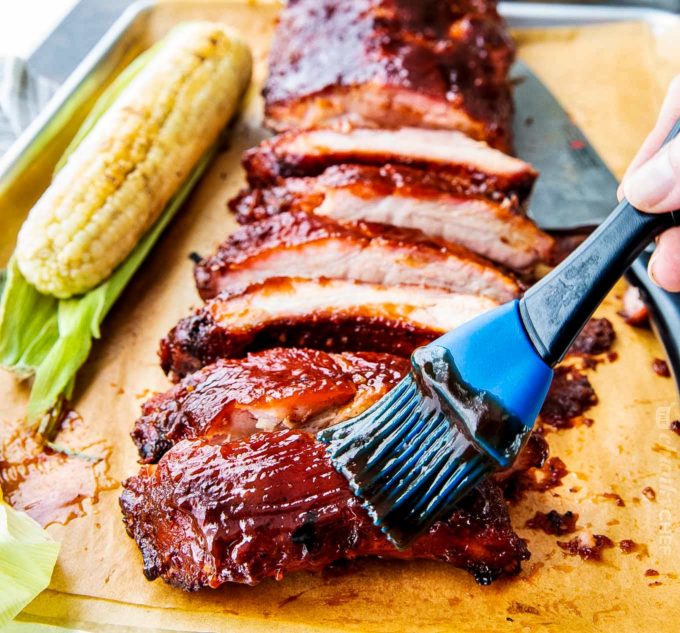 Delicious homemade smoked ribs are easier to make than you think, especially using the popular 3-2-1 method.ย Fall of the bone tender, and lip-smackingly good, these ribs are FABULOUS!! #ribs #pork #bbq #smoked #smoking #grilling #easyrecipe Brushing bbq sauce on smoked ribs