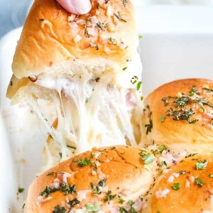 The ultimate party or finger food, these melt in your mouth ham and cheese sliders are made savory with the addition of garlic and herbs, drizzled in a garlic/shallot butter and baked until tender and golden! #appetizer #partyfood #fingerfood #sliders #hamandcheese #garlicandherb #easyrecipe