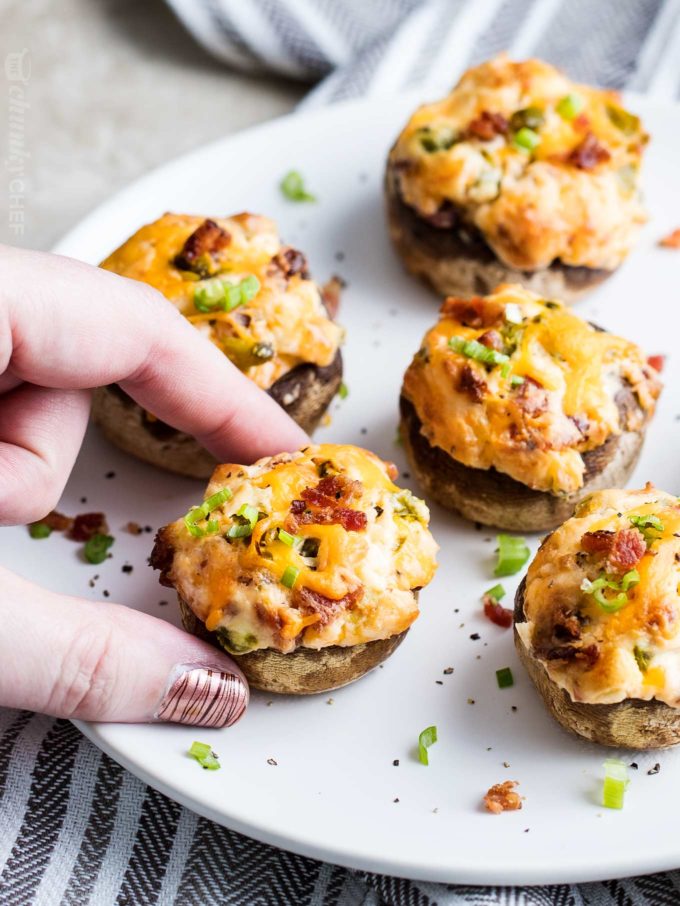 Grabbing a cheesy stuffed mushroom from white plate