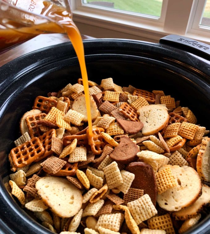 Pouring seasoned butter over chex mix in slow cooker