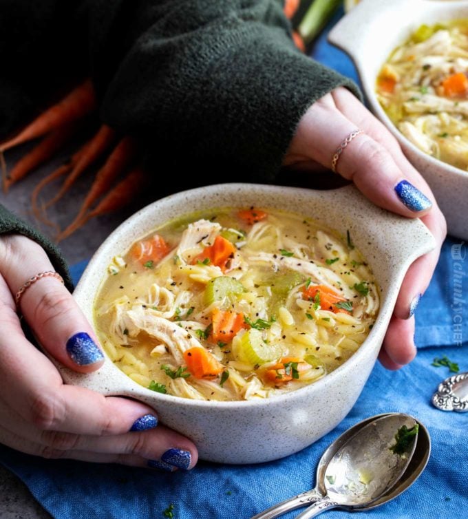 Hands holding a bowl of lemon chicken soup with orzo