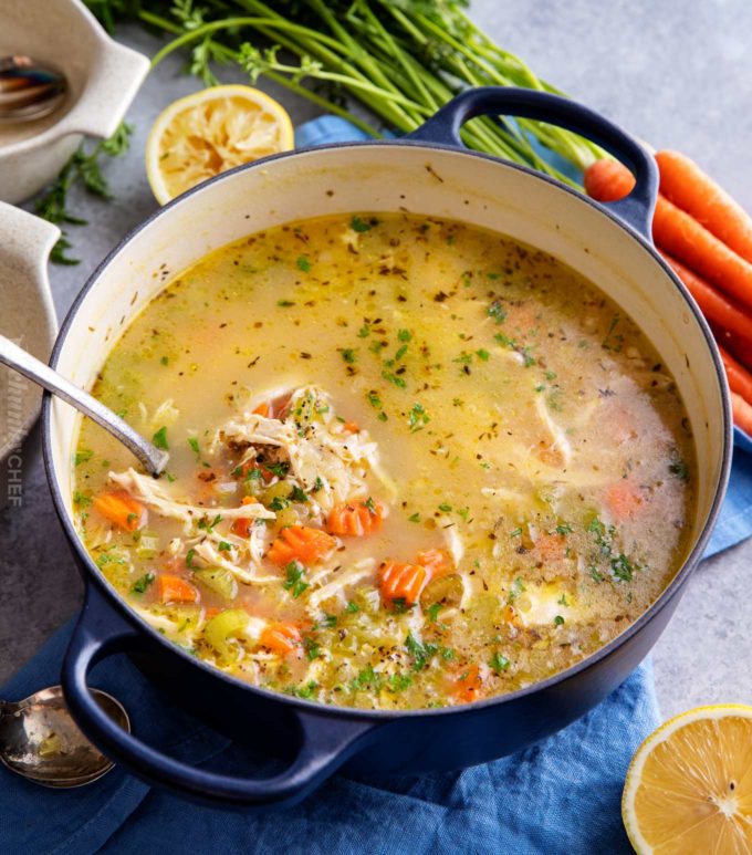 Ladle of lemon chicken soup with orzo in dutch oven pot