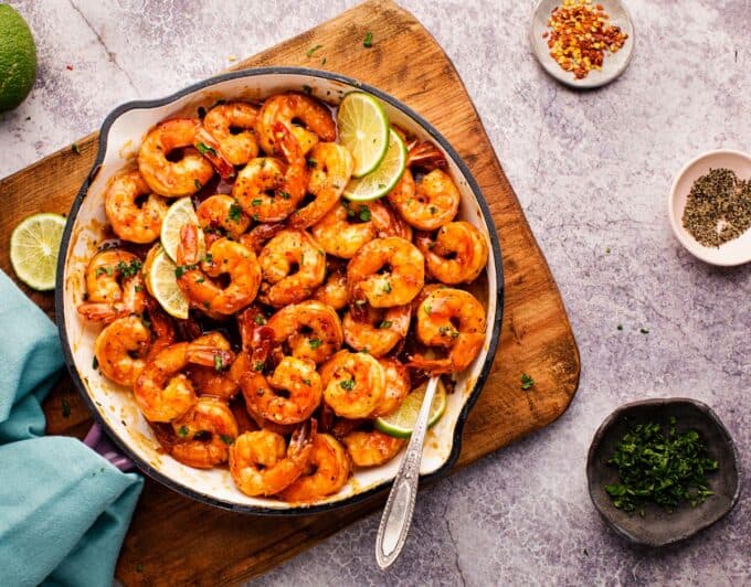 hot cast iron skillet with honey shrimp on a wooden cutting board.
