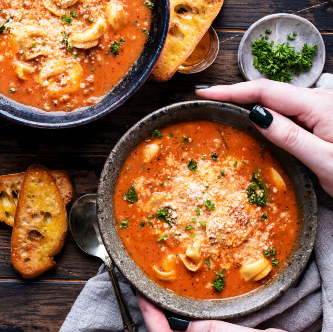 Two bowls of creamy tortellini soup with bread