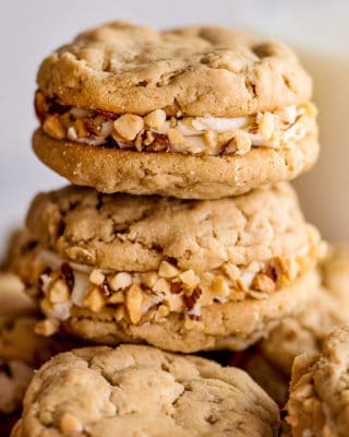 Chewy peanut butter cookies sandwiched together with rich buttercream, and rolled in crushed peanuts! It's a peanut butter lover's dream dessert! #peanutbutter #cookies #dessert #easyrecipe #baking #chewy #oatmeal #sandwich #homemade
