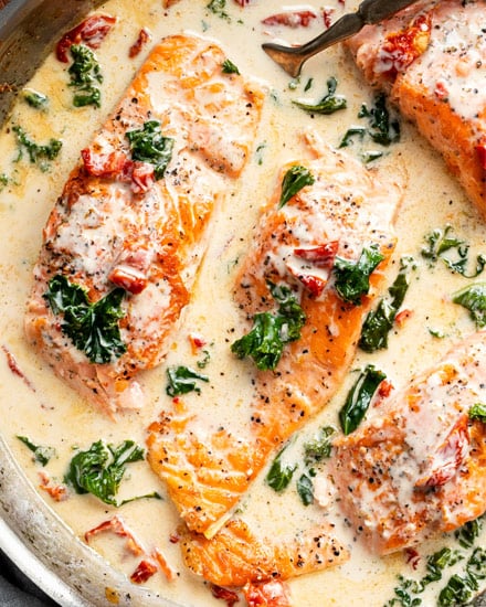 Tender salmon filets smothered in a rich garlic cream sauce filled with sun-dried tomatoes, kale and Parmesan cheese. Restaurant quality salmon, in 30 minutes! #salmon #seafood #fish #creamsauce #30minutemeal #easyrecipe #tuscan #Italian #sundriedtomatoes #kale #spinach