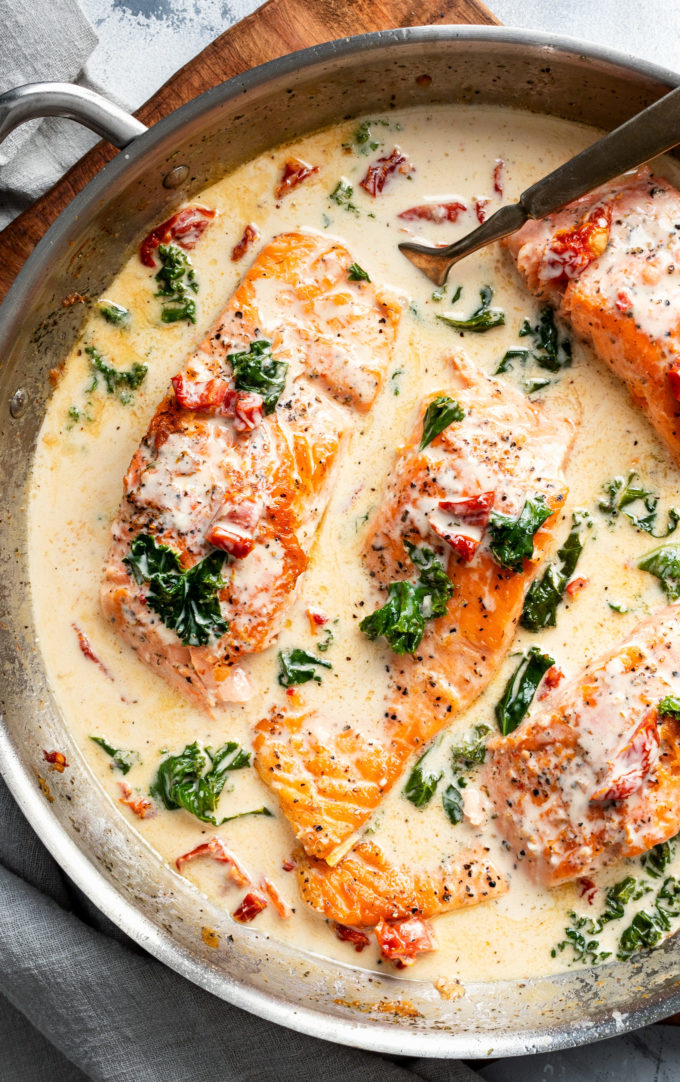 Tender salmon filets smothered in a rich garlic cream sauce filled with sun-dried tomatoes, kale and Parmesan cheese. Restaurant quality salmon, in 30 minutes! #salmon #seafood #fish #creamsauce #30minutemeal #easyrecipe #tuscan #Italian #sundriedtomatoes #kale #spinach