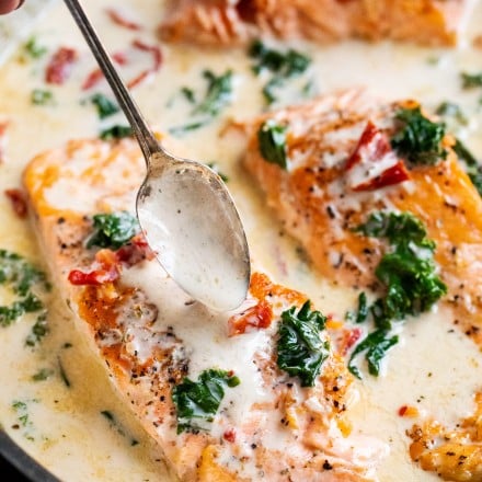 Tender salmon filets smothered in a rich garlic cream sauce filled with sun-dried tomatoes, kale and Parmesan cheese. Restaurant quality salmon, in 30 minutes! #salmon #seafood #fish #creamsauce #30minutemeal #easyrecipe #tuscan #Italian #sundriedtomatoes #kale #spinach