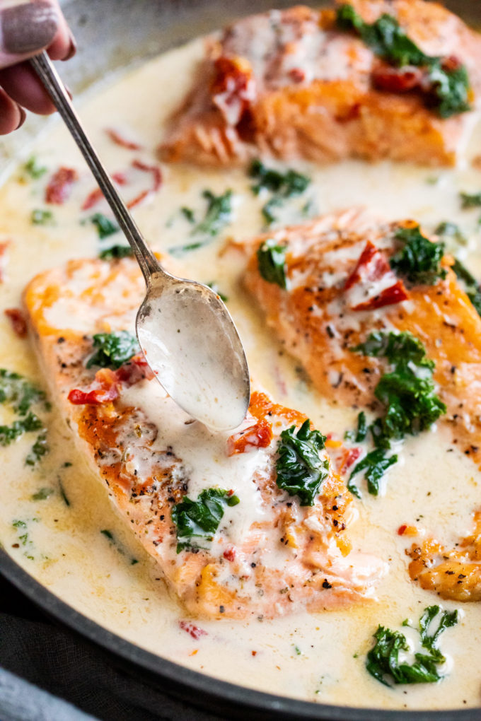 Tender salmon filets smothered in a rich garlic cream sauce filled with sun-dried tomatoes, kale and Parmesan cheese. Restaurant quality salmon, in 30 minutes! #salmon #seafood #fish #creamsauce #30minutemeal #easyrecipe #tuscan #Italian #sundriedtomatoes #kale #spinach