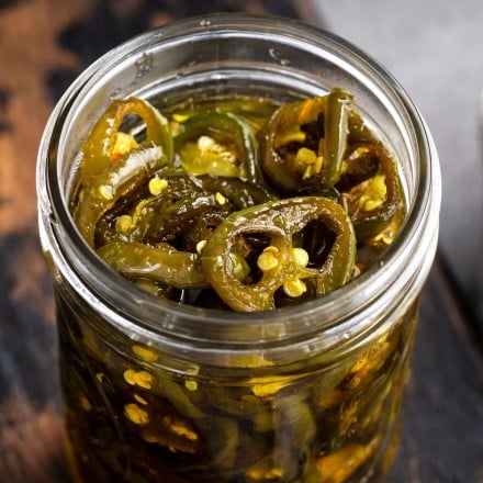opened jar of candied jalapenos on wooden cutting board