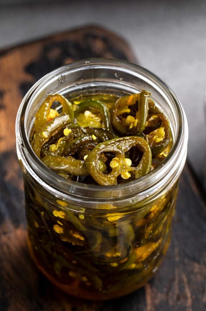 opened jar of candied jalapenos on wooden cutting board