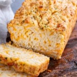 Sliced loaf of beer bread with cheese on wooden cutting board