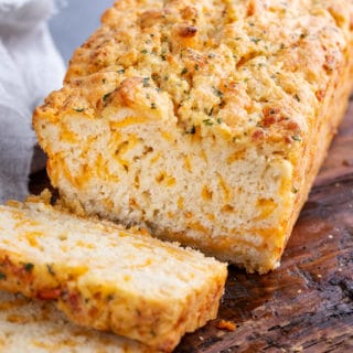 Sliced loaf of beer bread with cheese on wooden cutting board