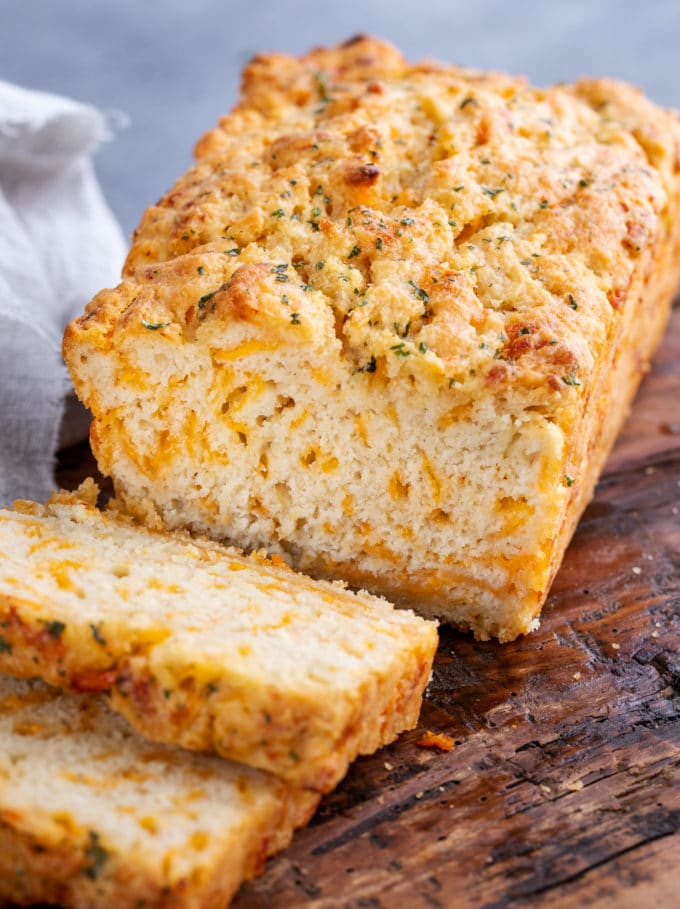 Sliced loaf of beer bread with cheese on wooden cutting board