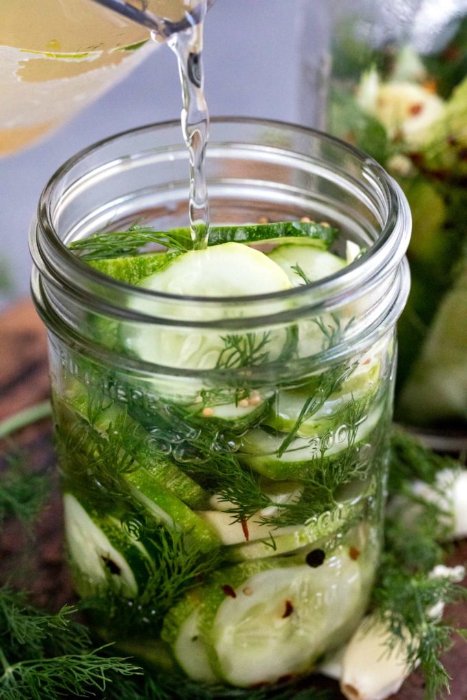 pouring brine into jar with cucumbers