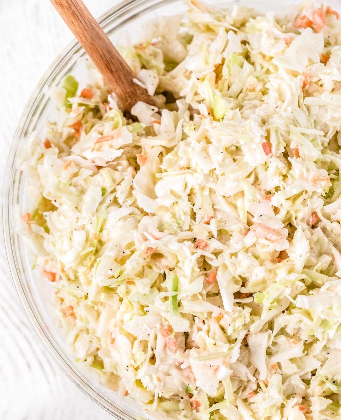 close up view of coleslaw in clear mixing bowl with wooden spoon