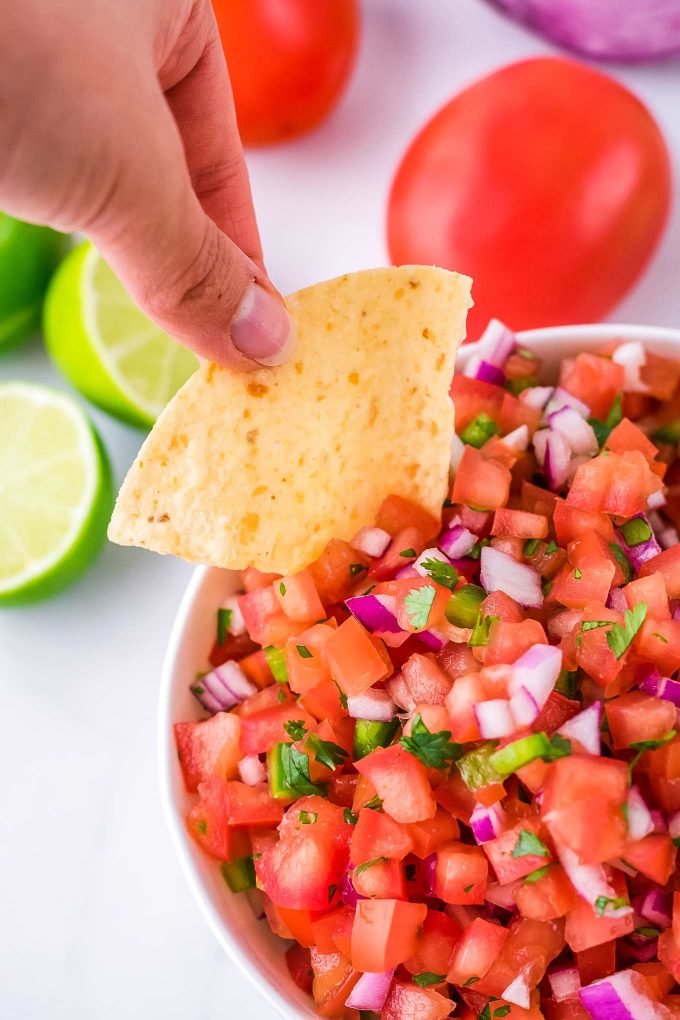 dipping a chip into a bowl of pico de gallo