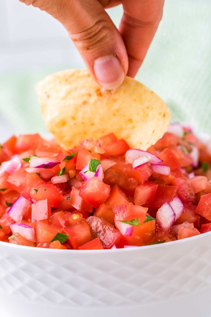 dipping a chip into a bowl of pico de gallo