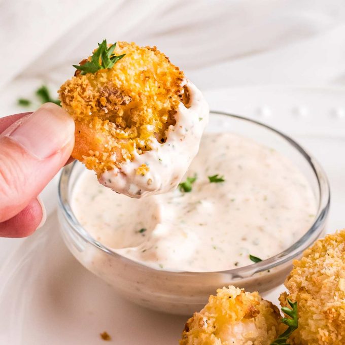 hand holding a piece of fried shrimp that's been dipped in remoulade sauce