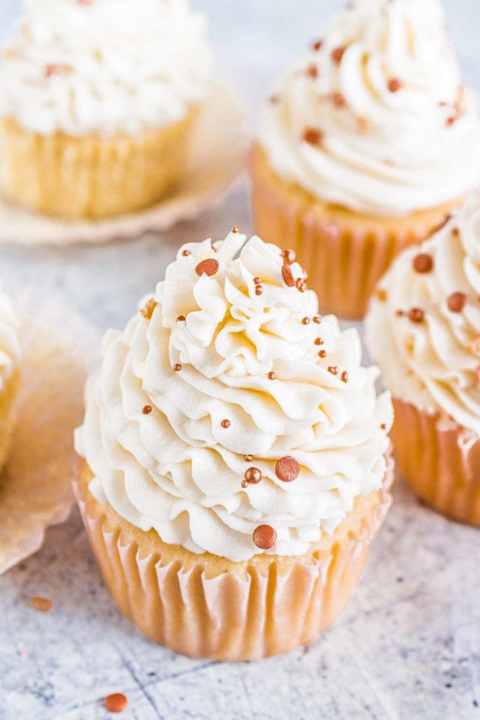 several vanilla cupcakes with frosting and sprinkles