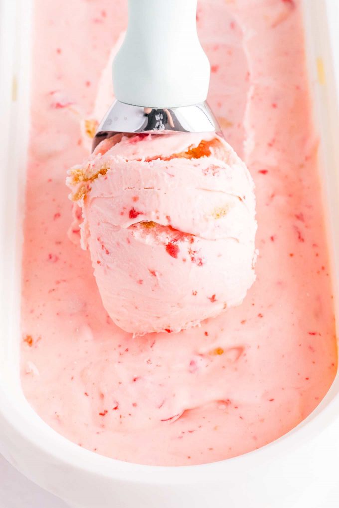 Scooping cherry ice cream out of ice cream tub with ice cream scoop