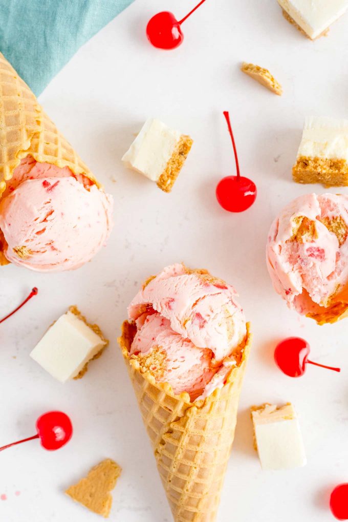 several waffle cones with cherry ice cream scattered with cherries and cheesecake pieces
