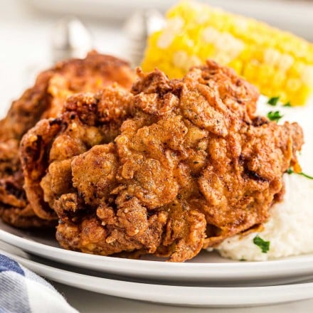 fried chicken thigh on plate with potatoes and corn